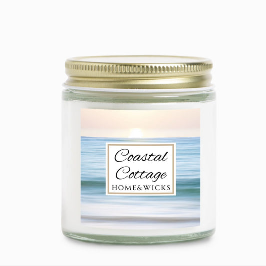 Coastal Cottage candle jar with a label reading 'Coastal Cottage' by 'Homes & Wicks' with a calm ocean shore image on a white background